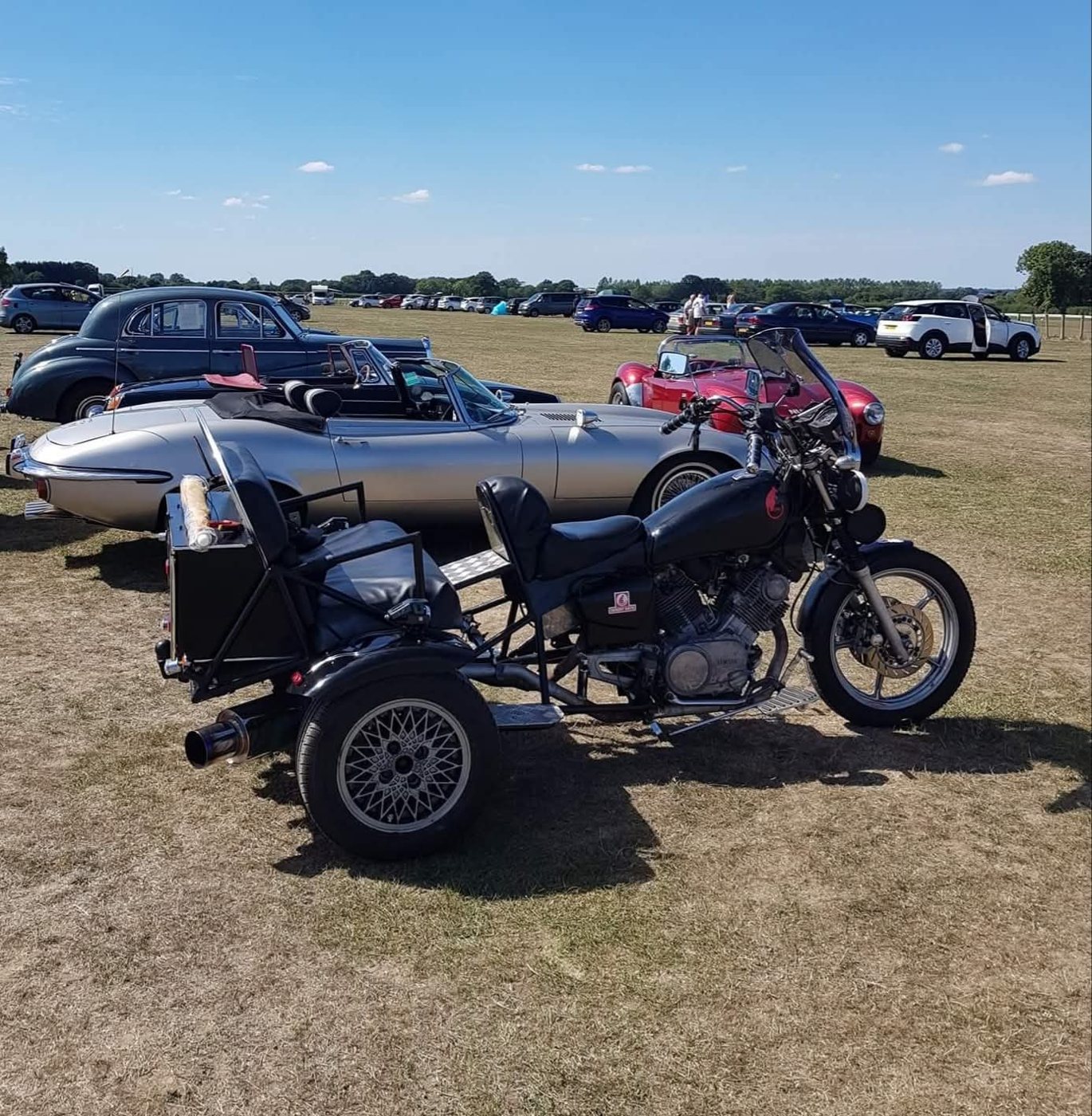 A black trike parked beside classic cars at a show